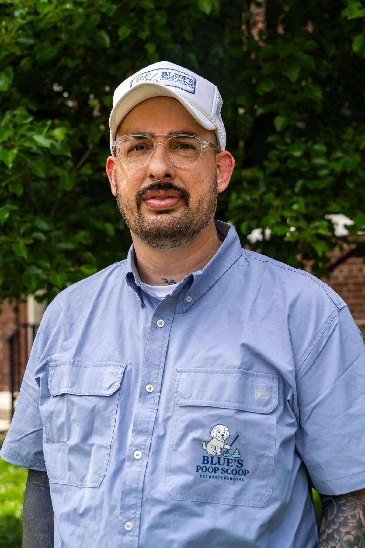 George, in a Blue's Poop Scoop cap and branded shirt, outside in front of a hedge