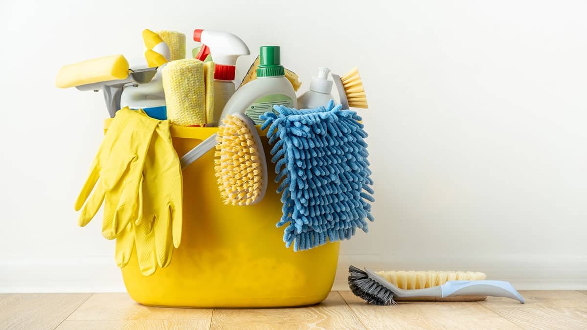 A yellow bucket packed with brushes, cloths, gloves and spray bottles