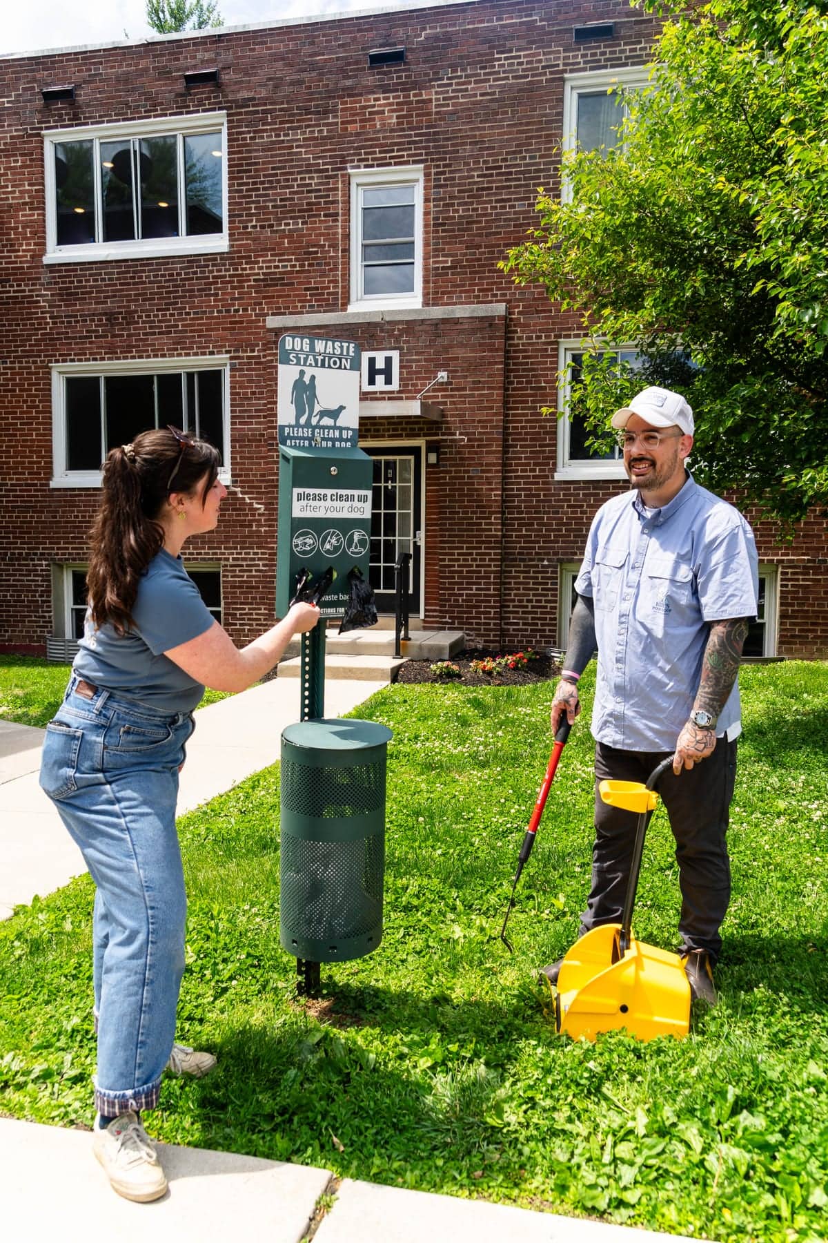 Two Blue's Poop Scoop staff beside a dog waste station, one holding a scooper