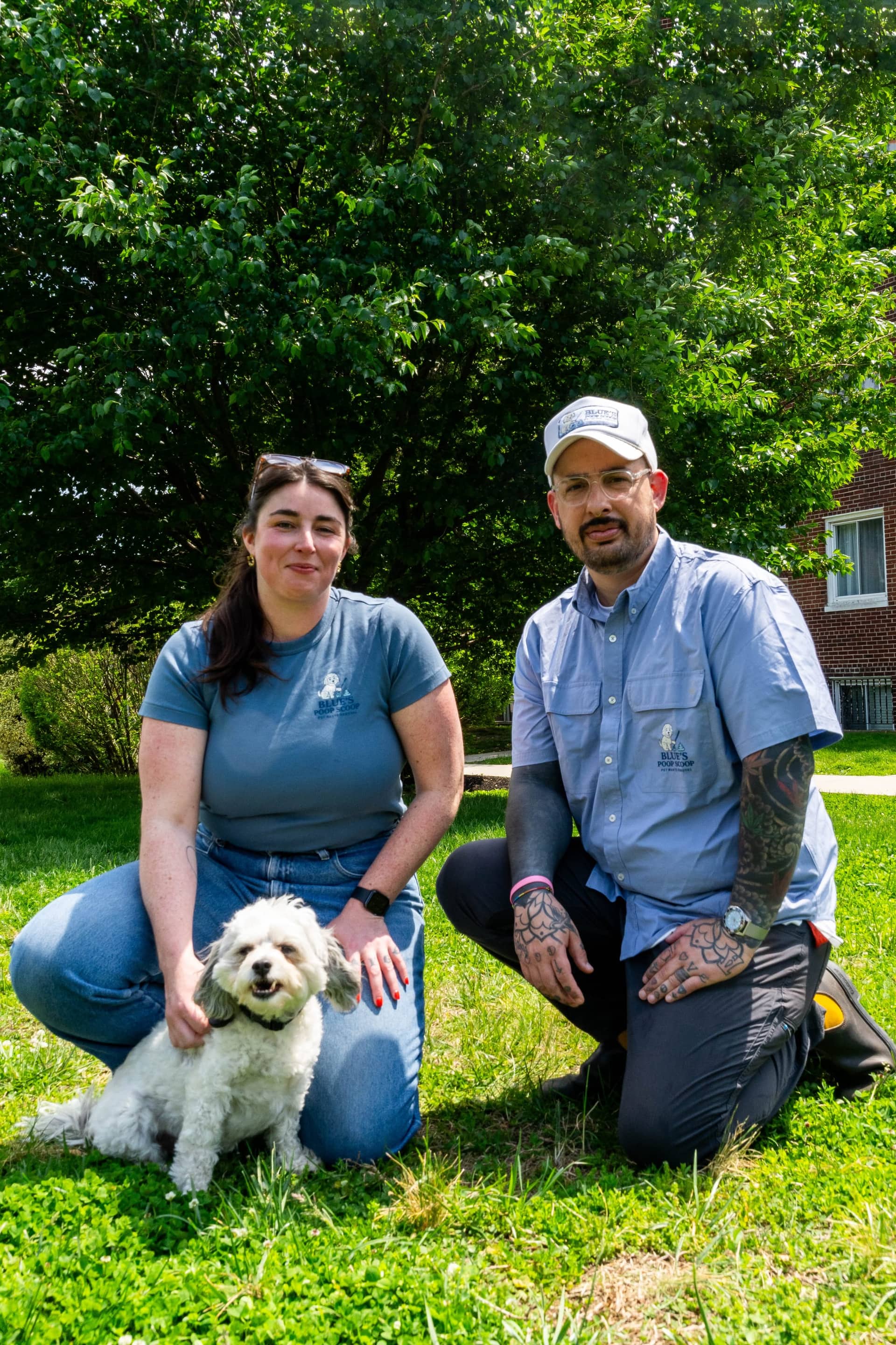 The owners of Blue's Poop Scoop kneeling on a lawn with their small white dog